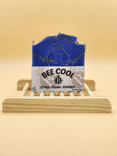 Blue bar of soap on a wooden stand with 'BEE COOL' label against a beige background