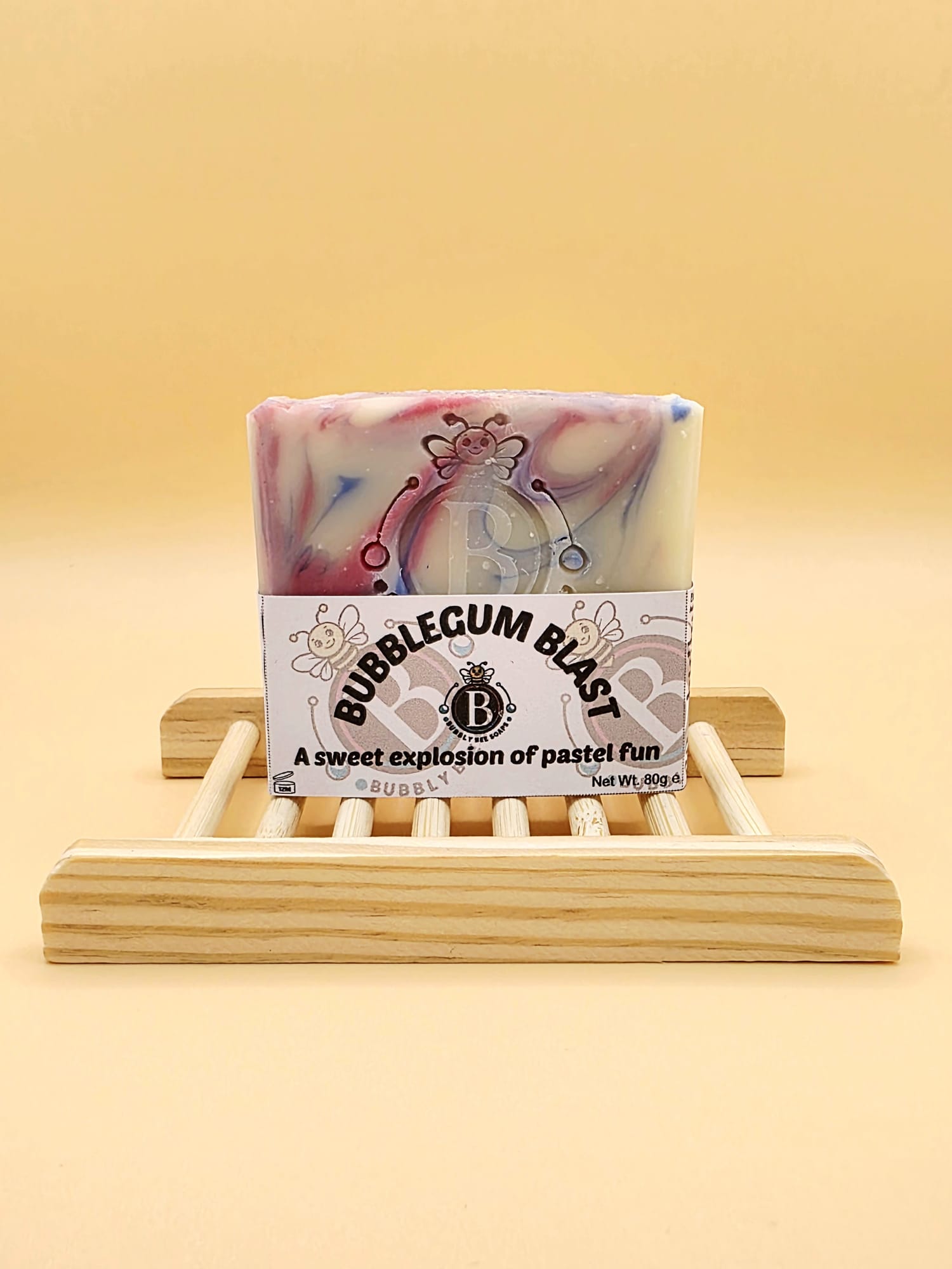 Bar of soap with 'Bubblegum Blast' packaging on a wooden stand against a yellow background